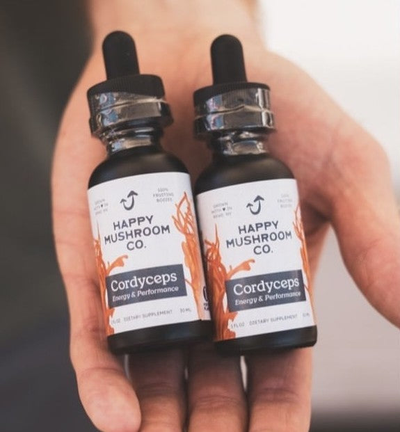 Hand holding two cordyceps mushroom tincture bottles in palm.